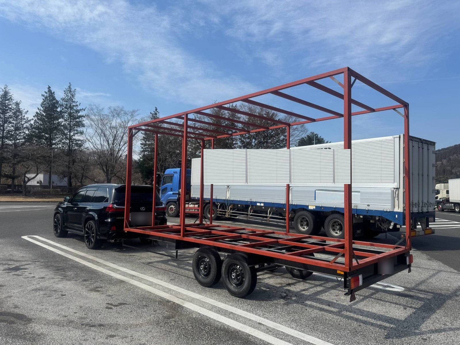 シャーシの上に赤い鋼製の外装フレーム（外枠）だけを組み上げた状態を、牽引車で搬送する様子（実例写真）
